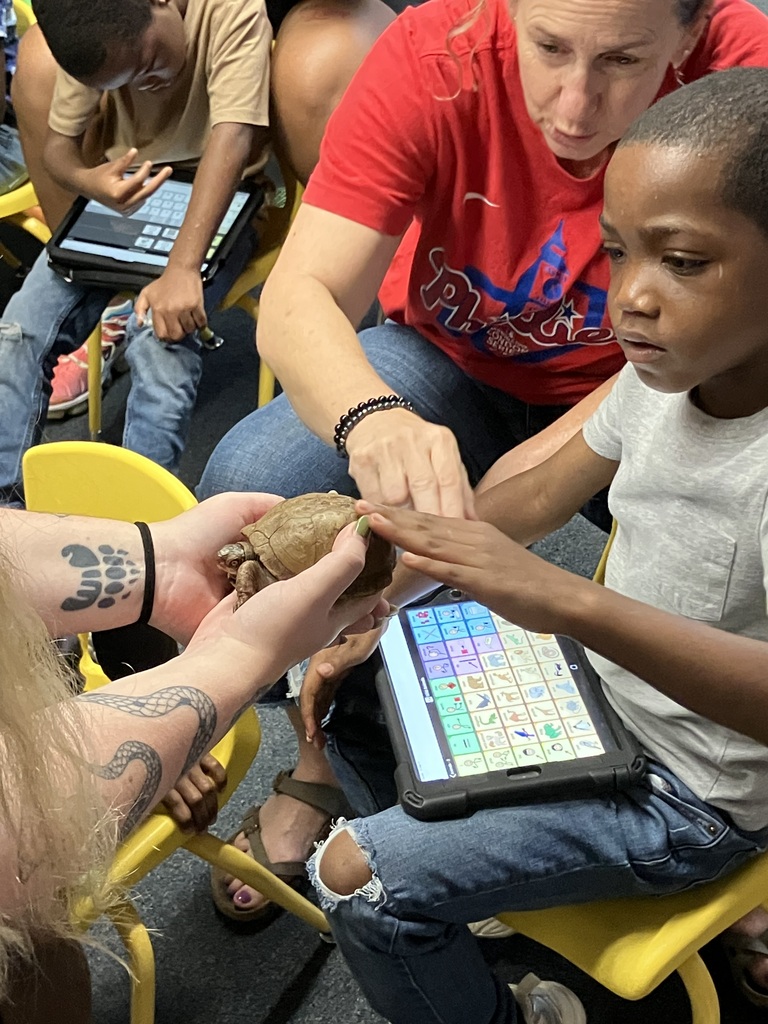 teacher helping a student holding an AAC device touch a turtle on the shell