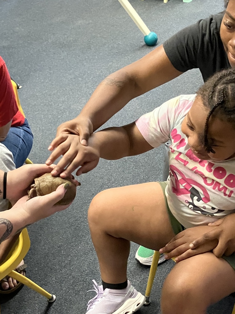 adult helping a student carefully touch a turtle on the shell while student smiles
