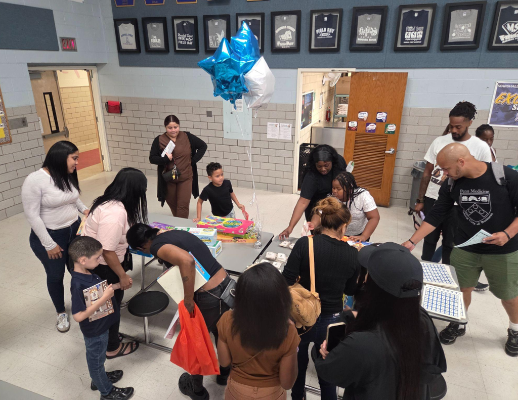 A group of parents and children browsing tables filled with colorful books during a Back-to-School Night event.