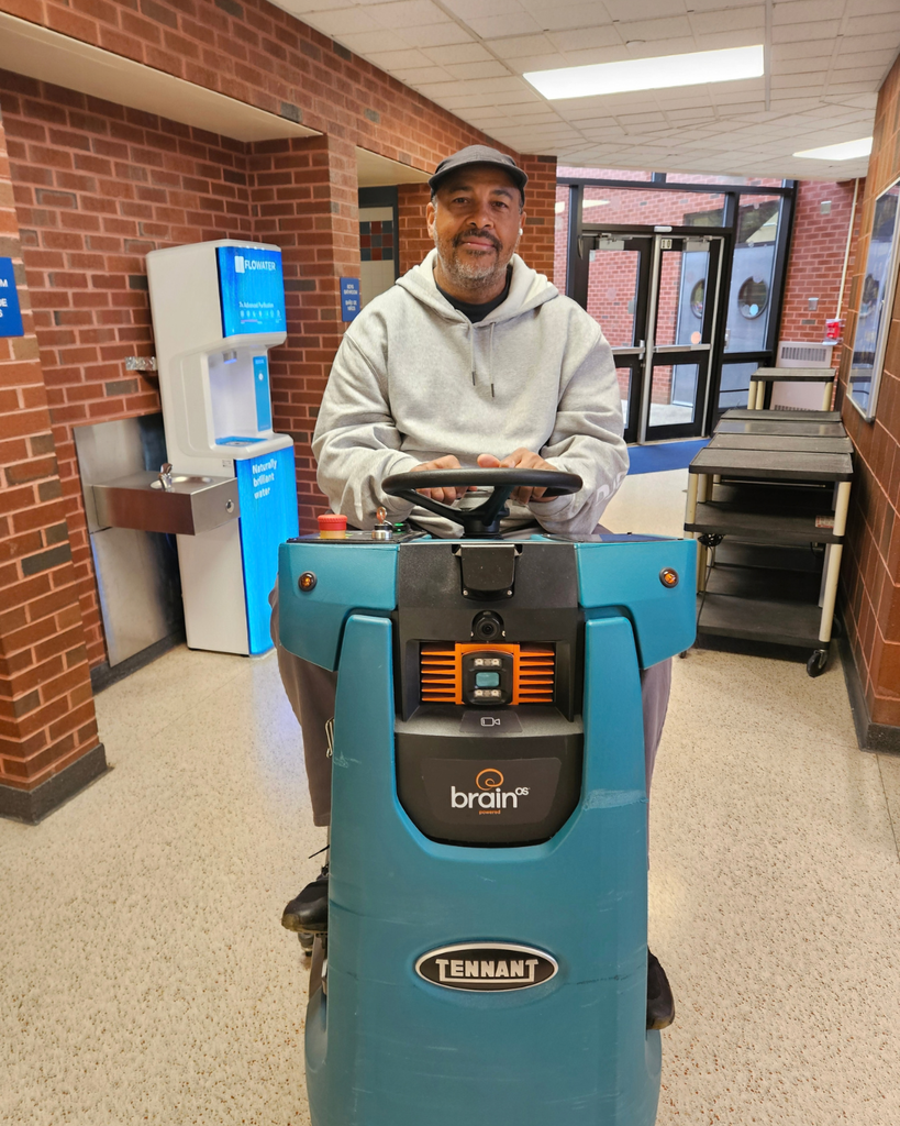 Custodian smiles for photo while on floor cleaning machine.
