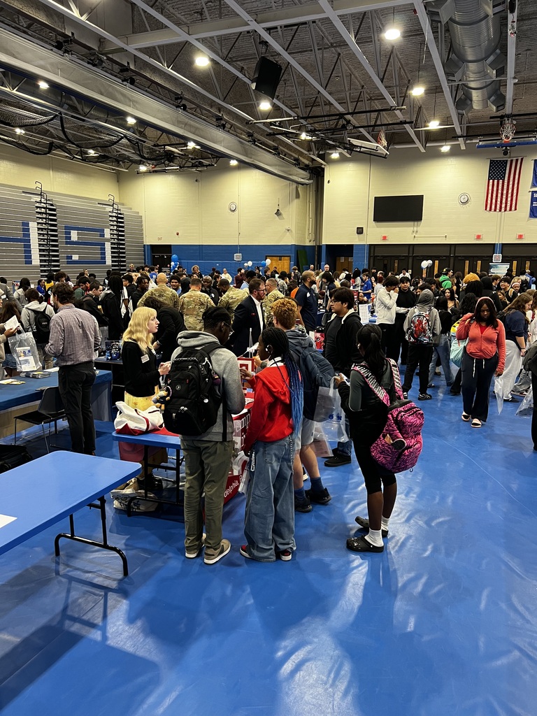 A large photo of students gathered in the gym walking around the vendors who are there to talk to them about college and careers