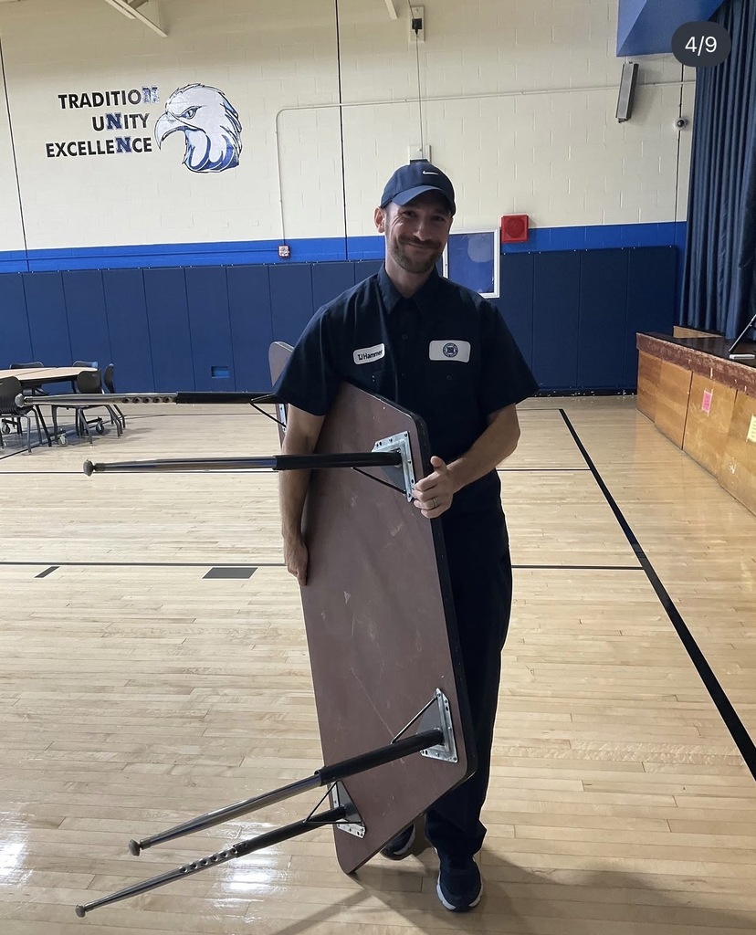 The head custodian is moving a table in the cafeteria