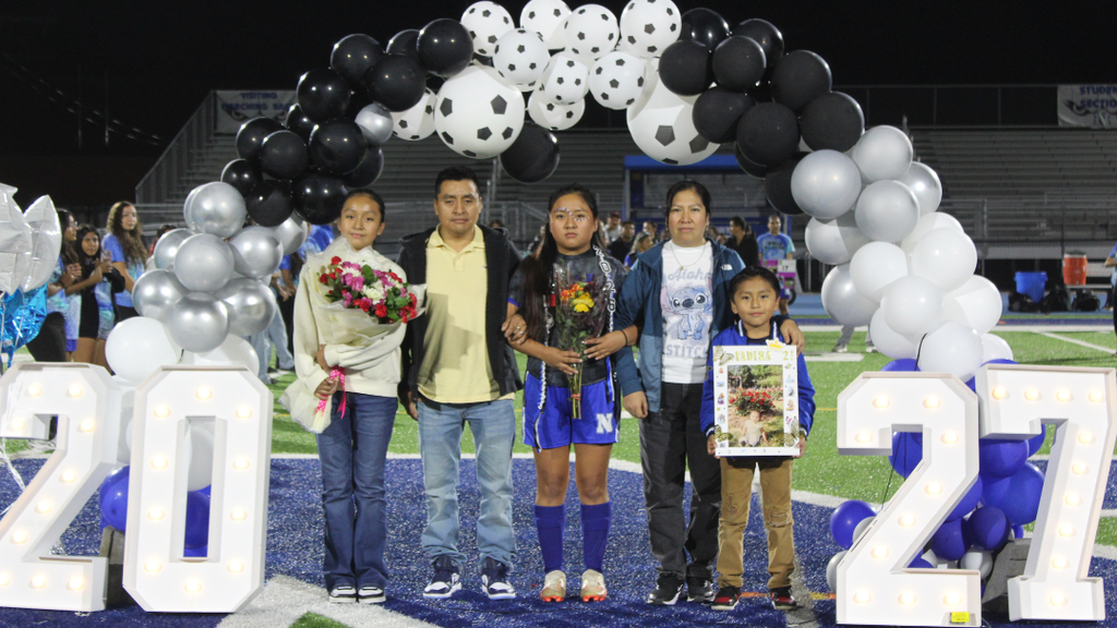 Senior athlete and family pose for photo under balloon arch.