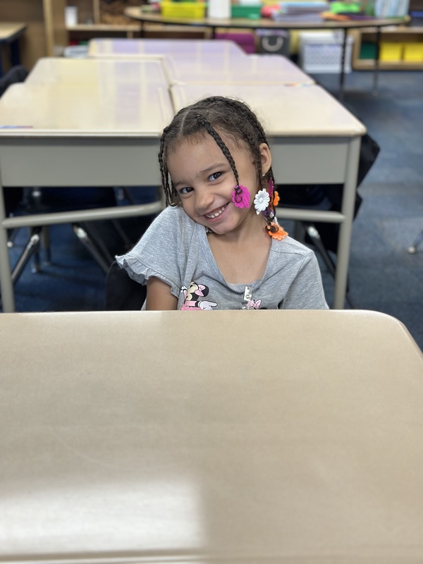 Kindergarten student smiling while sitting at classroom desk.
