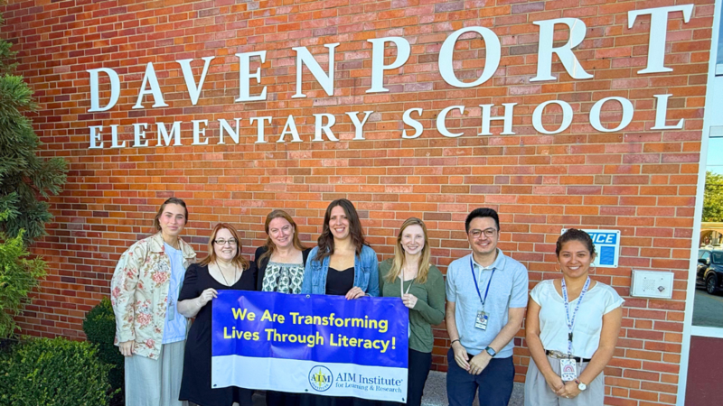 Davenport Staff pose for photo with AIM Institute Banner that says "We are transforming lives through literacy."