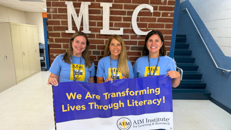 Musselman Staff pose for photo with AIM Institute Banner that says "We are transforming lives through literacy."