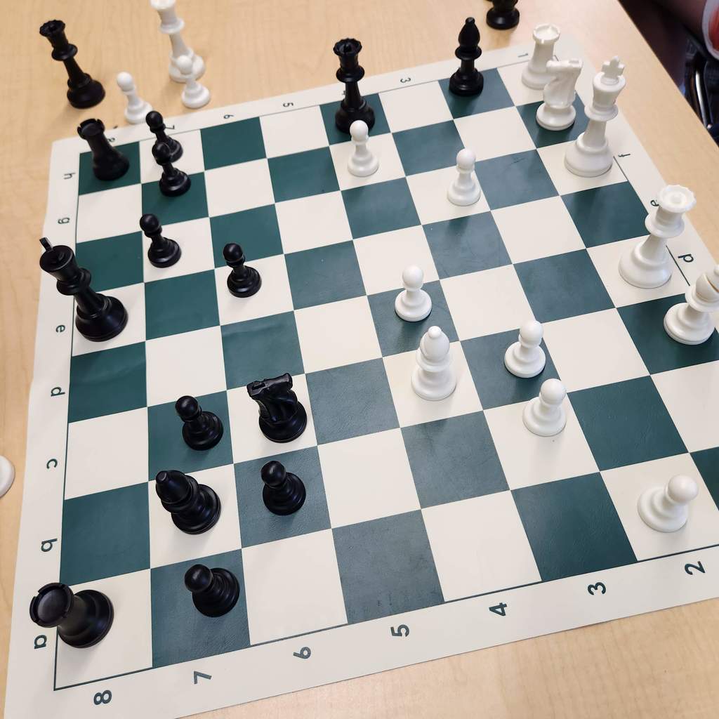 A green and white chess board with black and white pieces partway through a game.