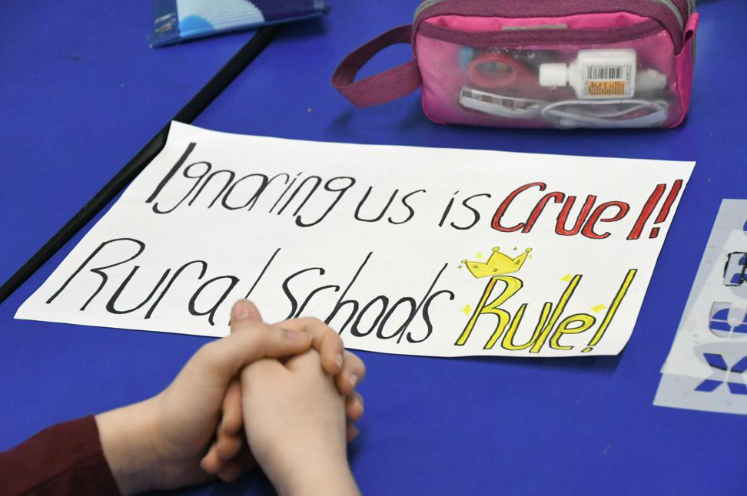 student poster that reads "ignoring us is cruel! rural schools rule!"