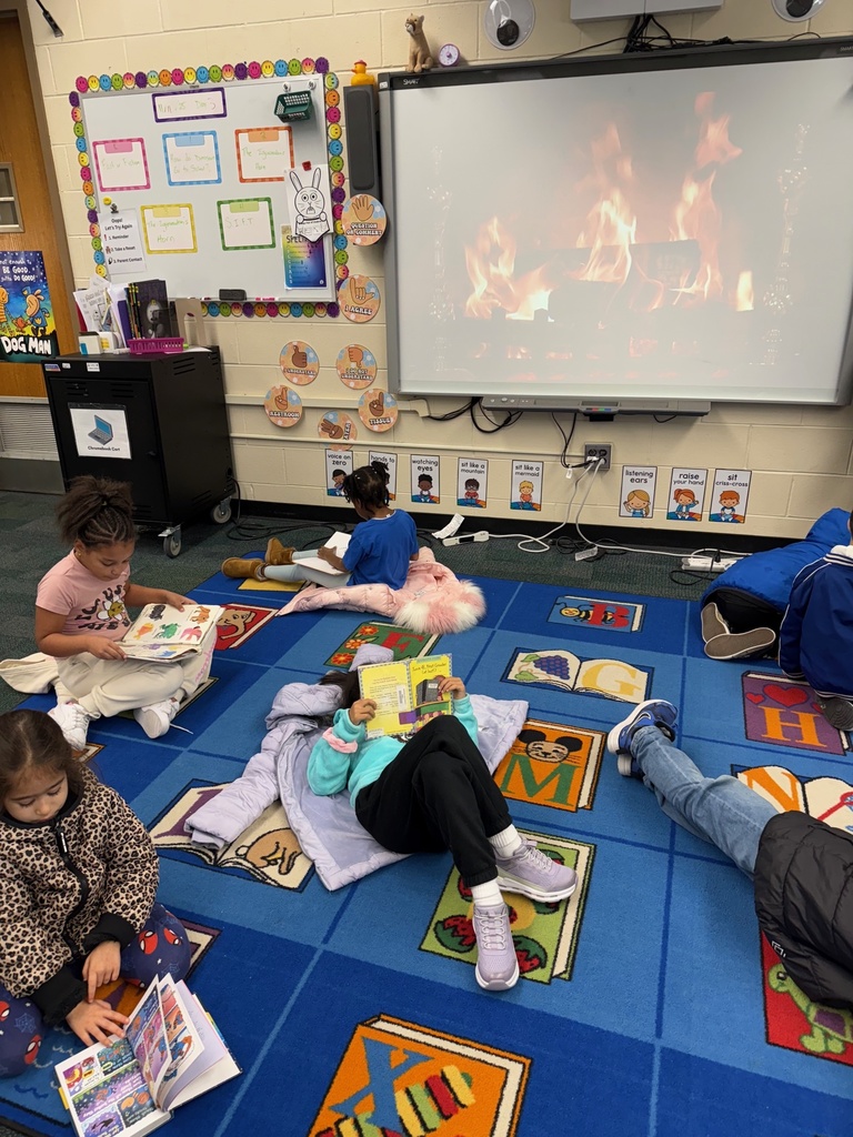 First grade students read books next to a yule log video