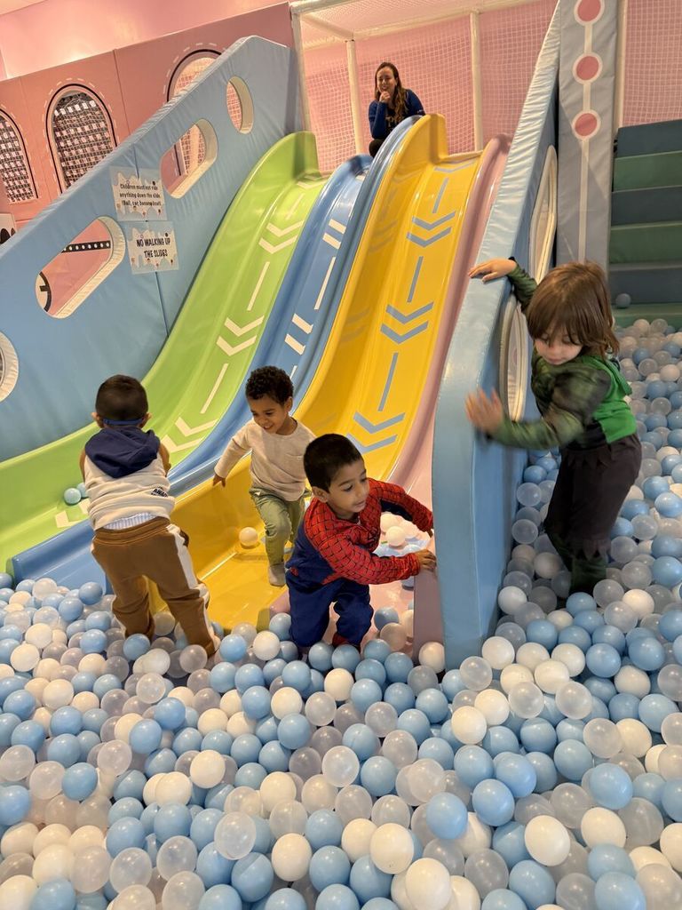 four boys play in the ball pit at the bottom of 4 slides