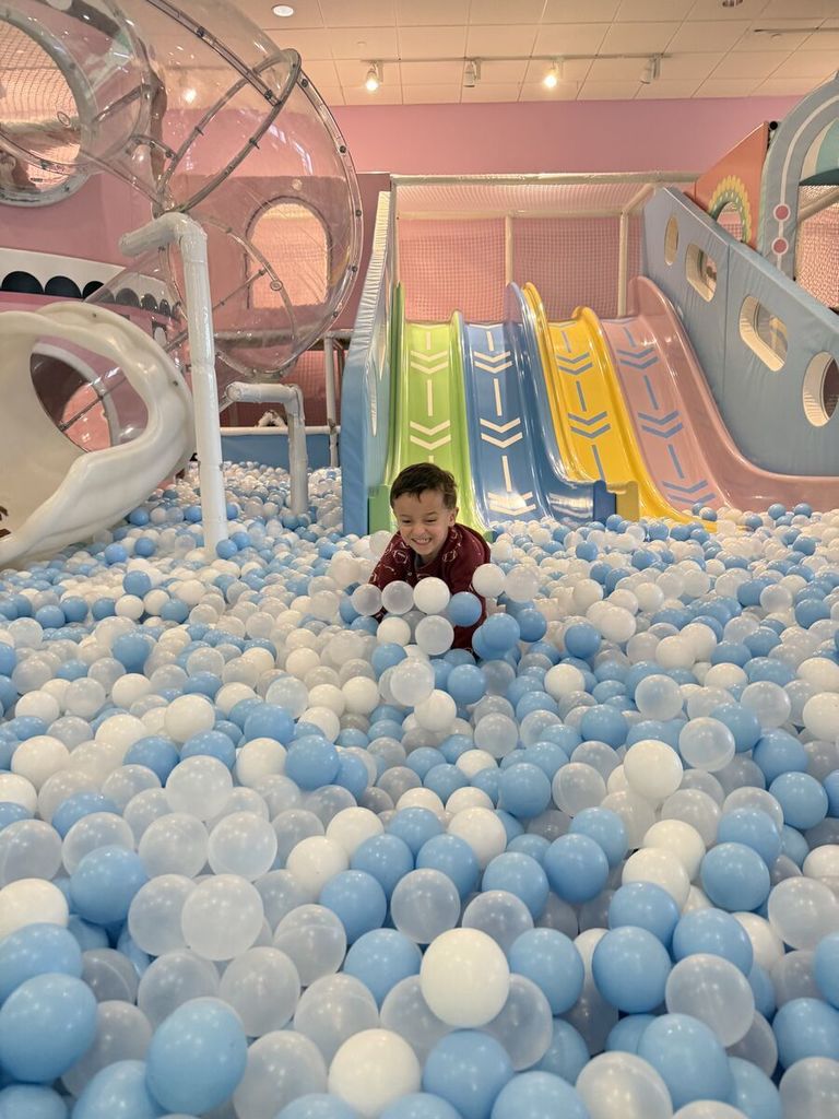 boy smiles widely at the bottom of the slide in a ball pit