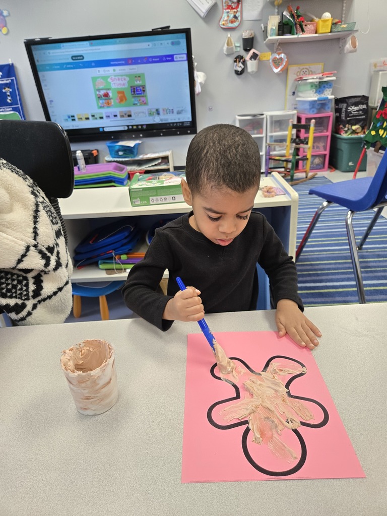 a young boy adds paint to the bottom of his gingerbread man with a large paint brush