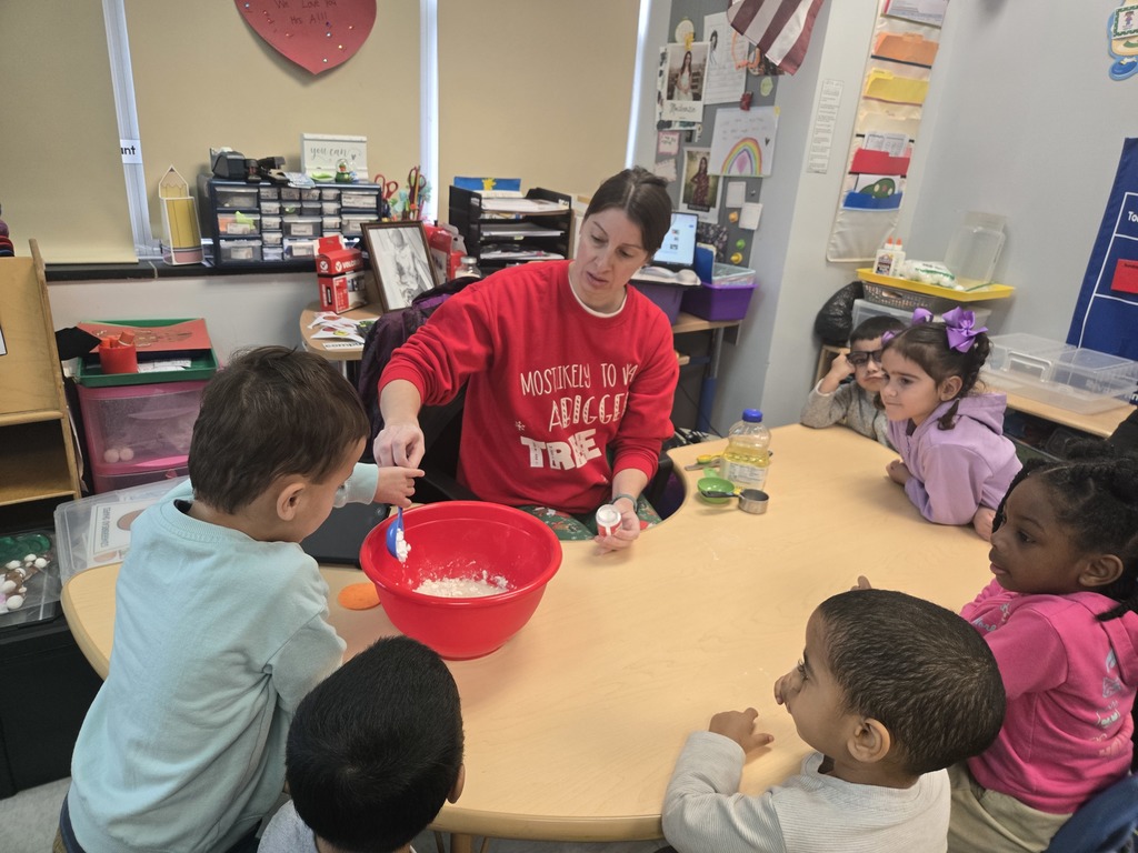 preschool students at a horse shoe table watch on as a peer pours an ingredient into the bowl