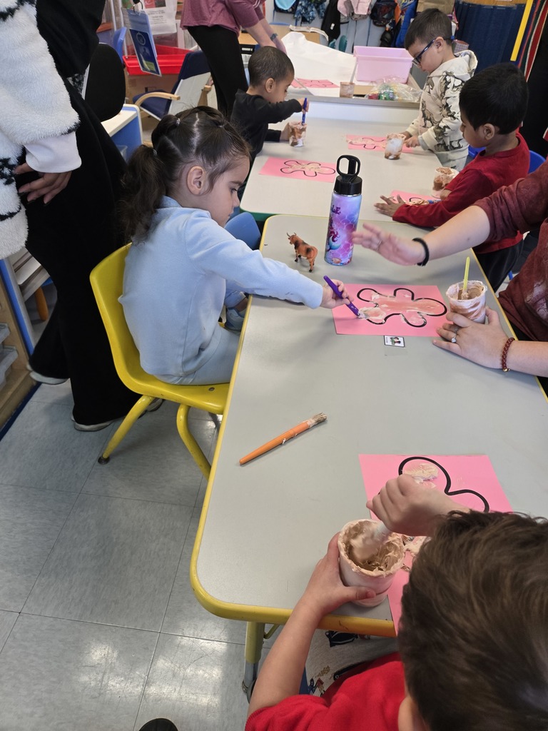preschool students sitting at a long table paint pink gingerbread men with brown fluffy paint