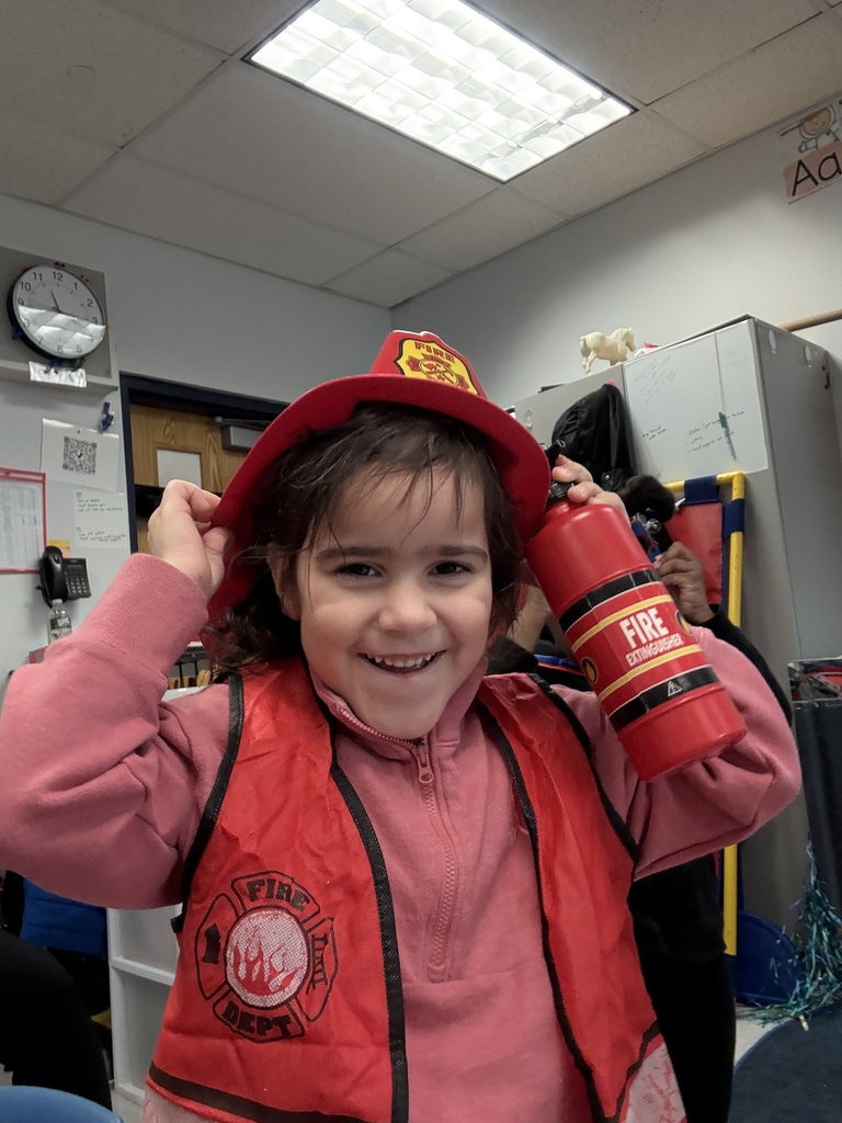 A preschool student smiles widely dress up in a firefighter vest and hat