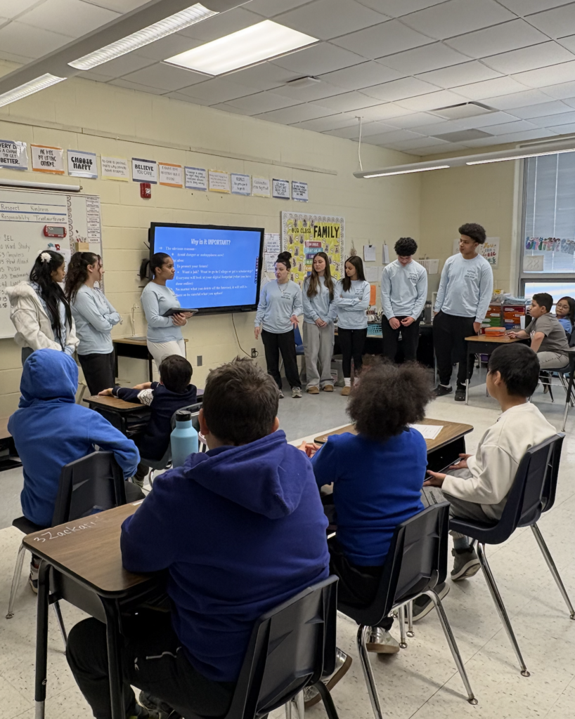Group of students presenting at front of elementary students in classroom