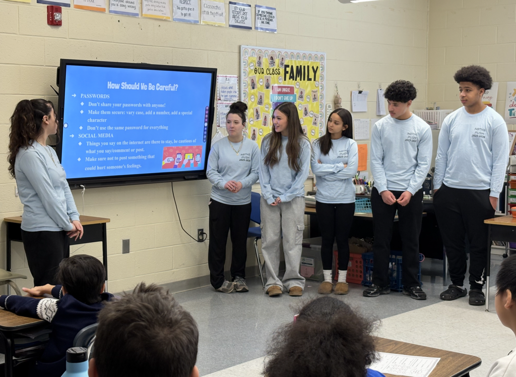 Group of students presenting at front of elementary students in classroom