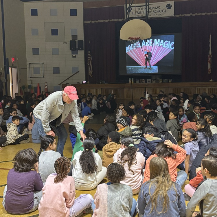 Man high fiving a group of students sitting on a gym floor
