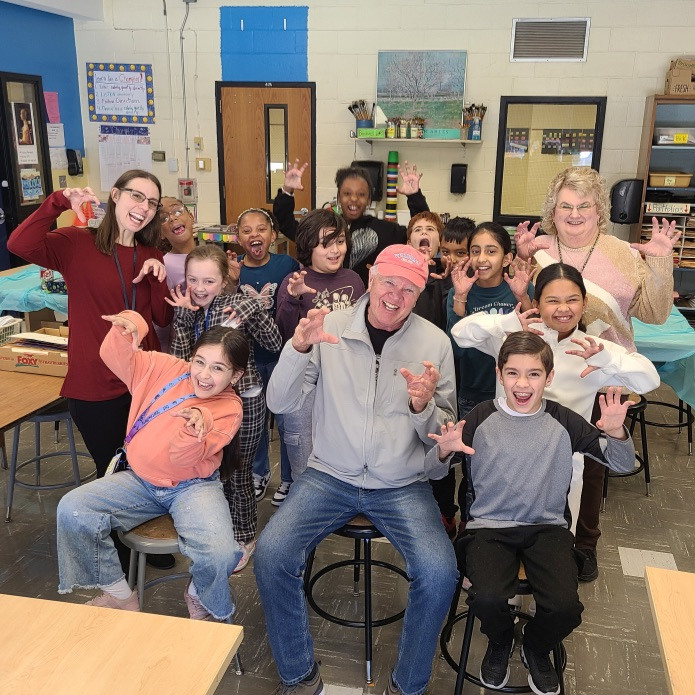 Group of students sitting together with several adults making funny faces