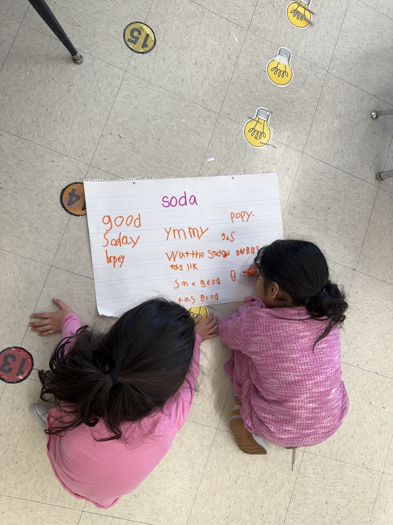 .Students working on poster board on the floor, writing words phonetically