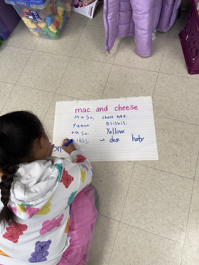 Student working on poster board on the floor, writing words phonetically