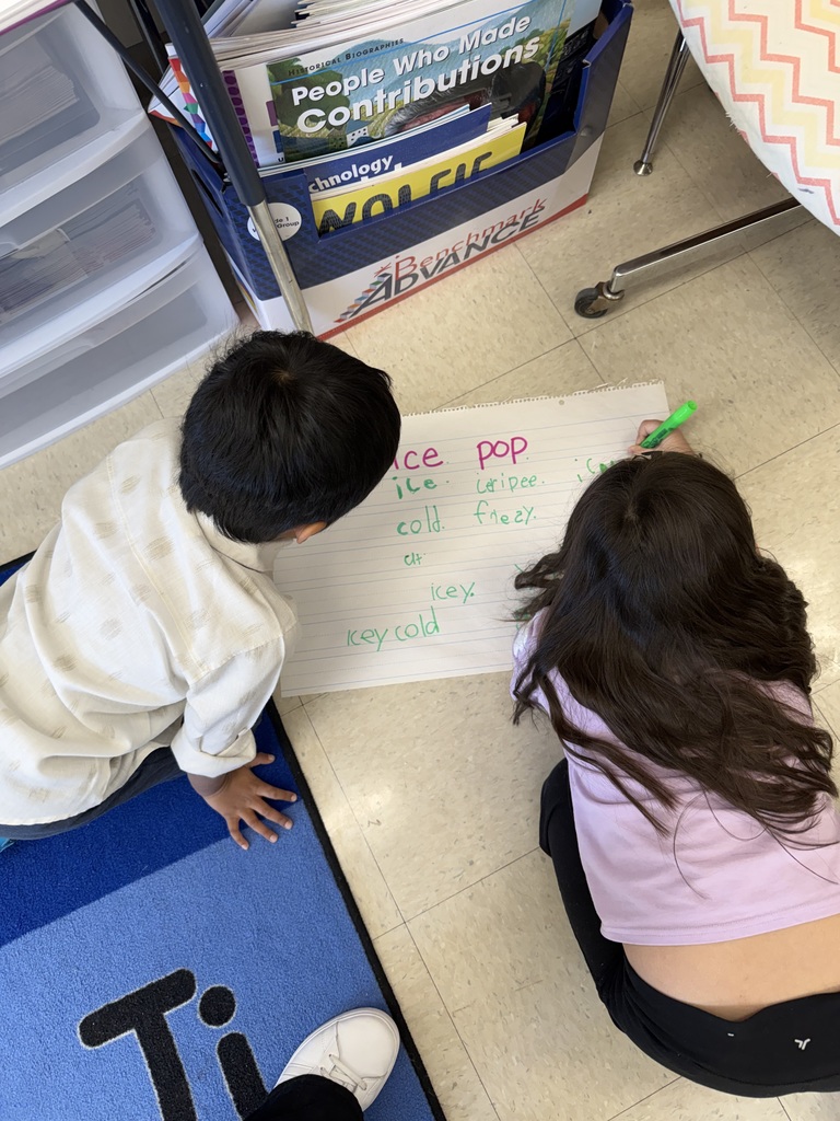 Students working on poster board on the floor, writing words phonetically