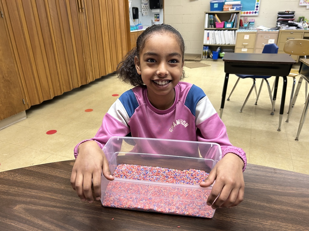 A student smiles while holding a bin of rice for finger spelling
