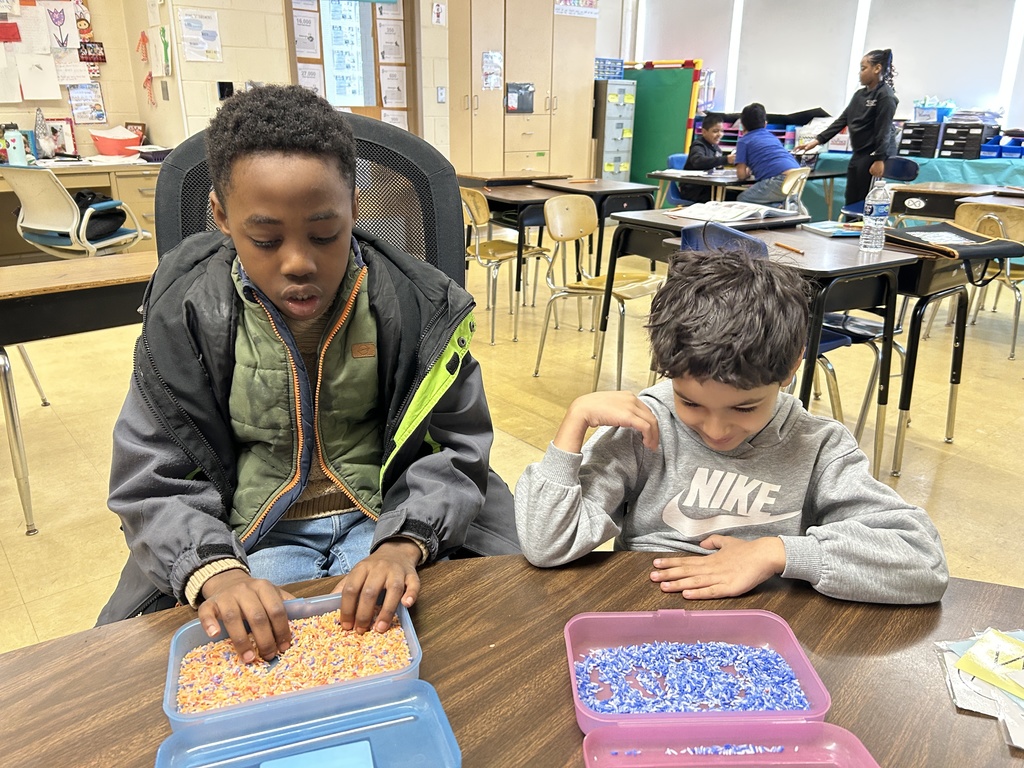 Two students are using bins of rice to finger write