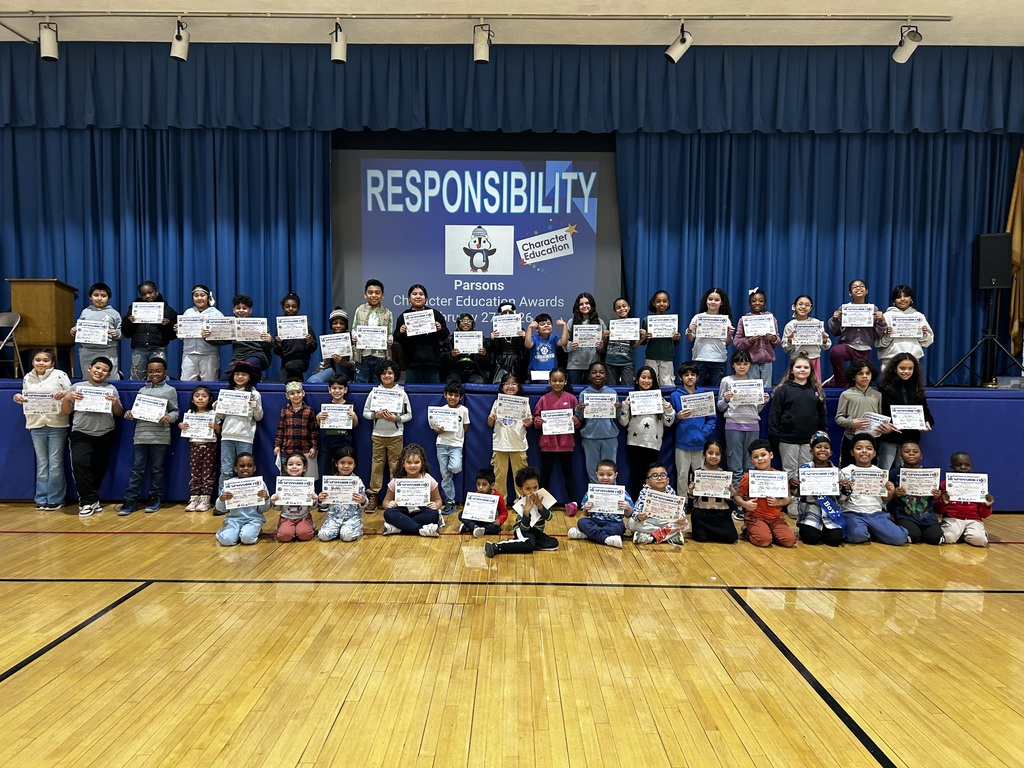 Photo of student assembly with elementary kids holding certificates in front of a screen title Responsibility