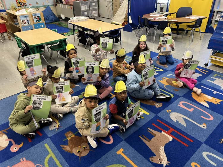 Students holding community helper books sitting on a classroom carpet.