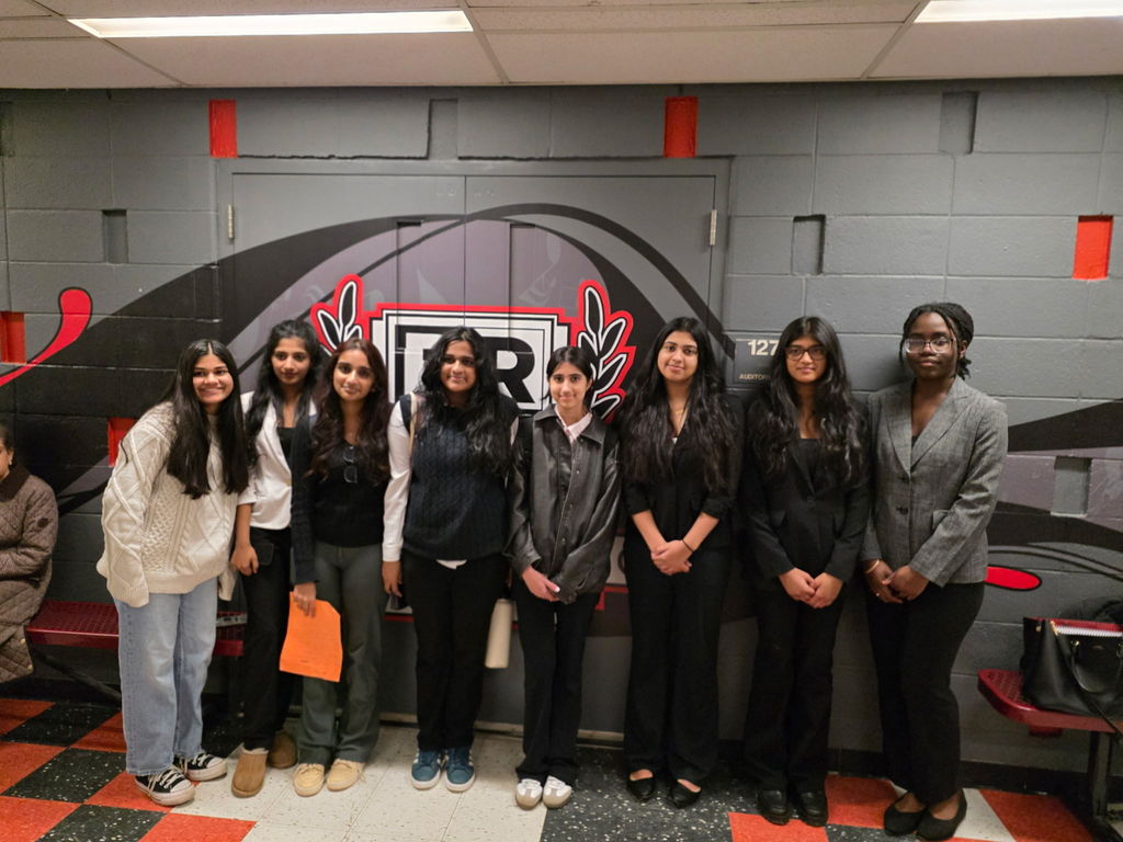 Eight members of the Speech & Debate Club stand in front of a mural by the Bridgewater-Raritan High School auditorium.