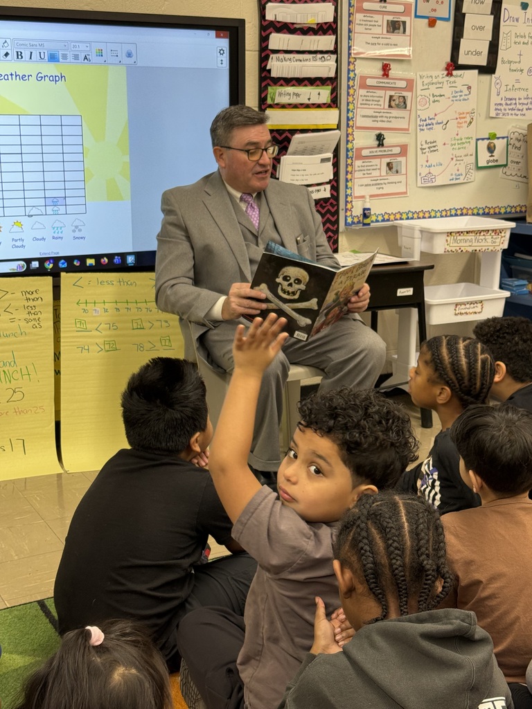 Adult reads a book to students sitting on the floor of a classroom