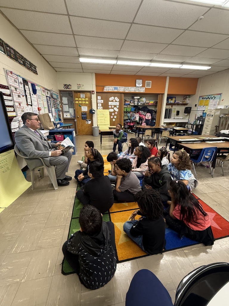 Adult reads a book to students sitting on the floor of a classroom