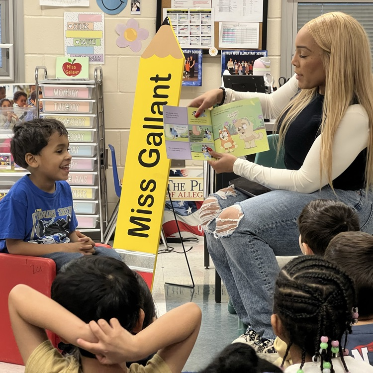 Students listening to an adult read a book in a classroom