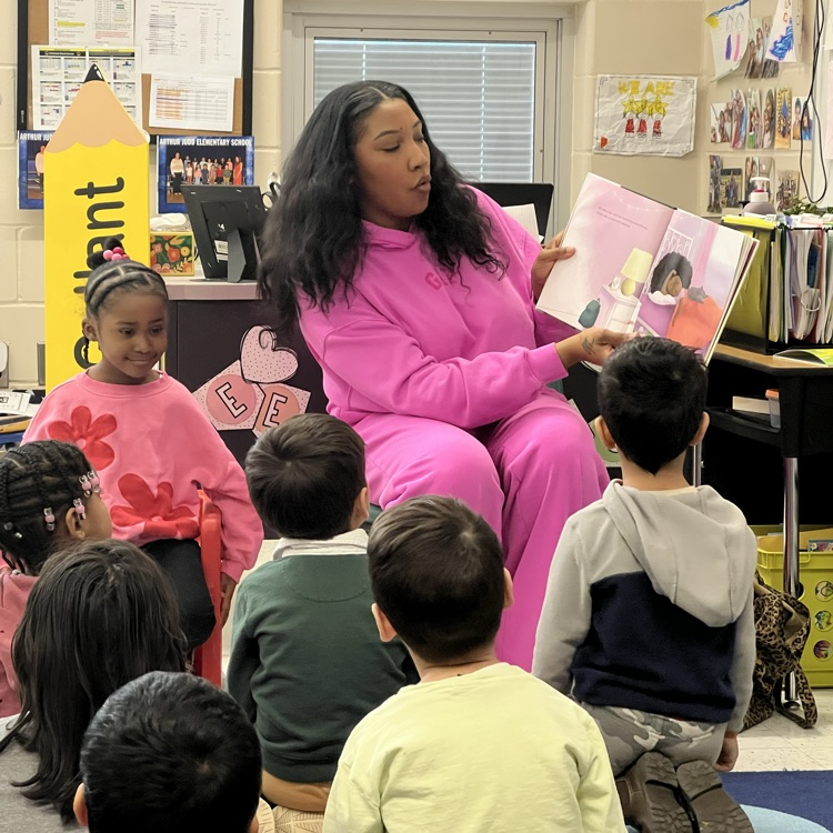 Students listening to an adult read a book in a classroom