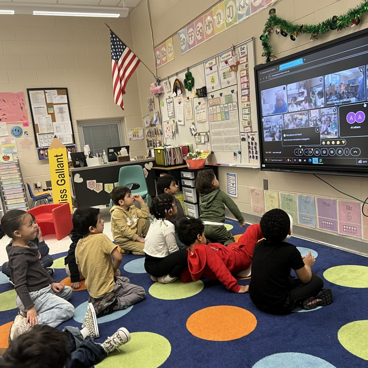 Students listening to an adult read a book in a classroom