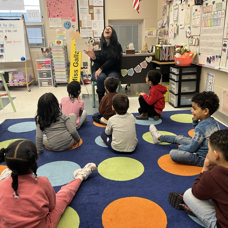 Students listening to an adult read a book in a classroom