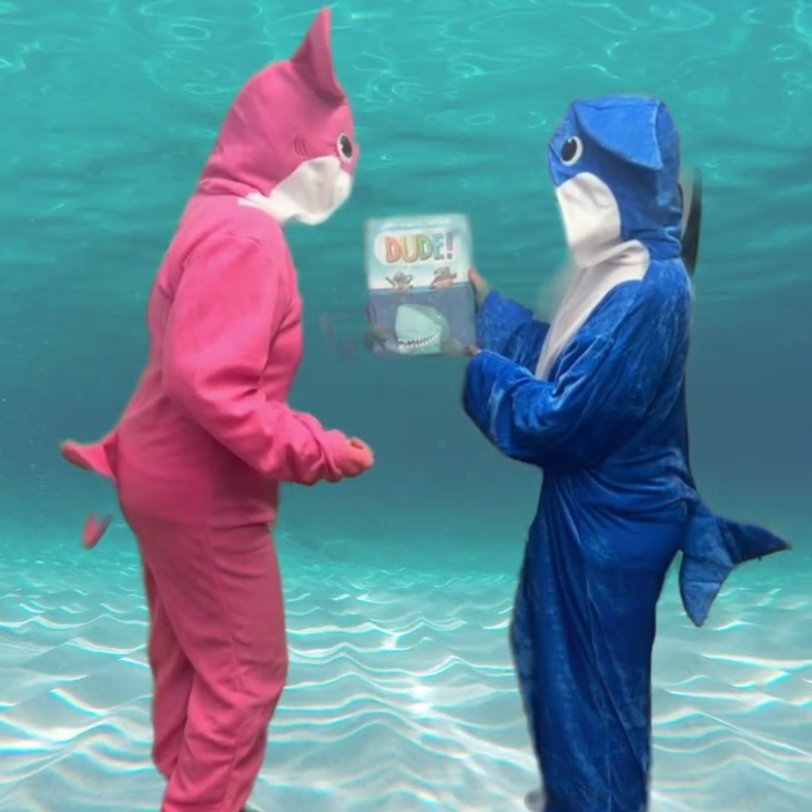 Two people in shark costumes with a book