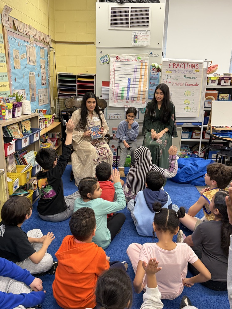 Students listening to an adult reader in their classroom