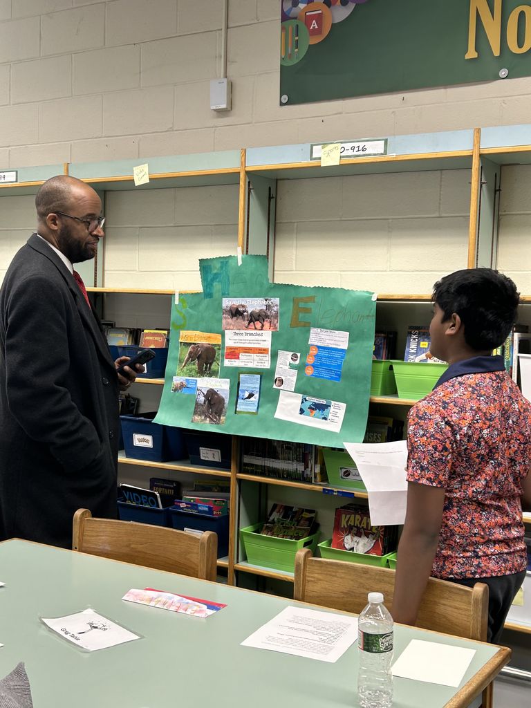 Student shares project with adult in classroom library