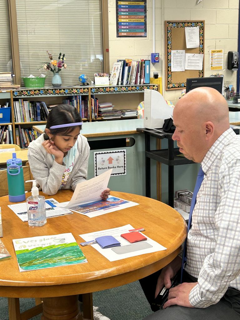 Student shares project with adult in classroom library