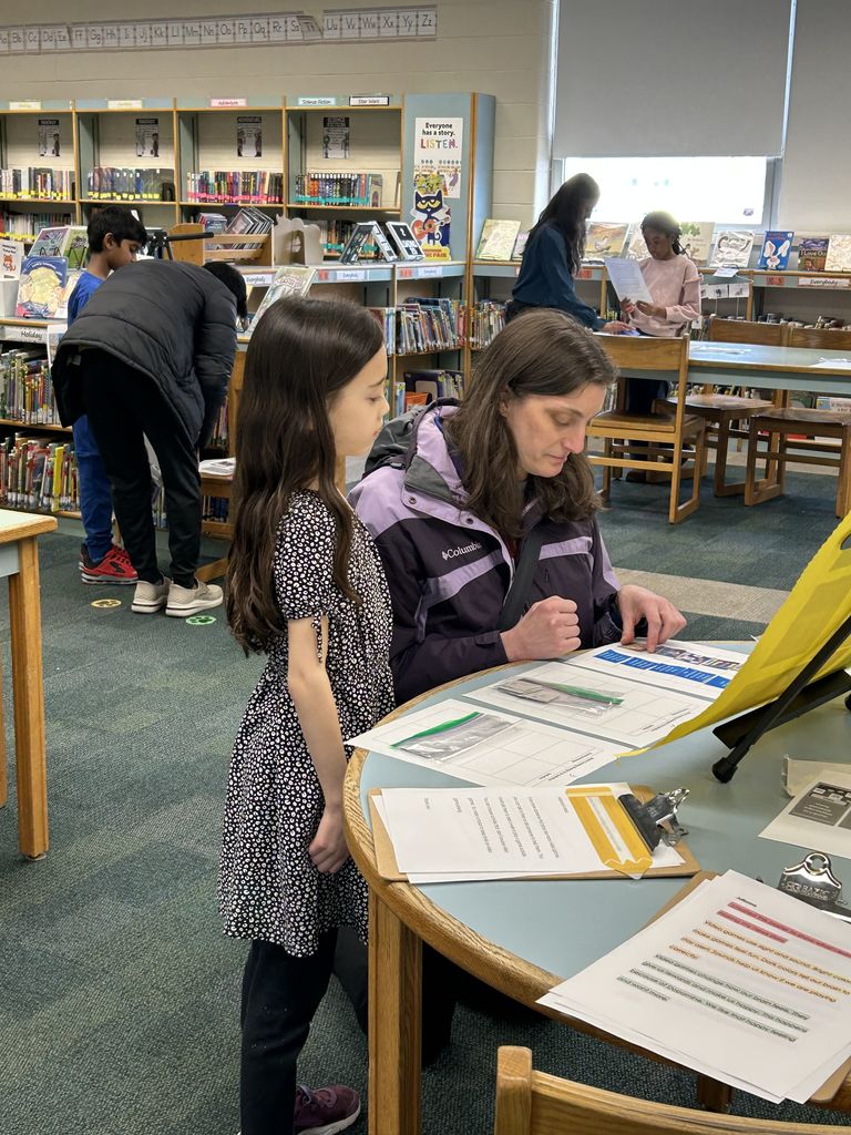 Student shares project with adult in classroom library