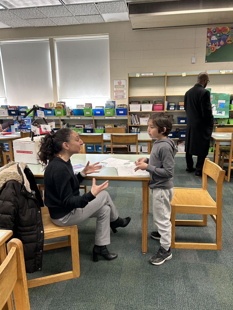 Student shares project with adult in classroom library