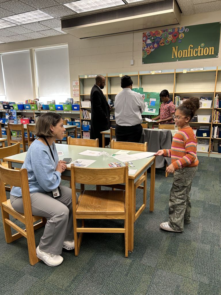 Student shares project with adult in classroom library