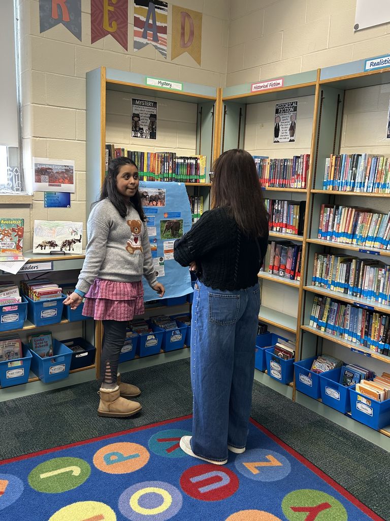 Student shares project with adult in classroom library