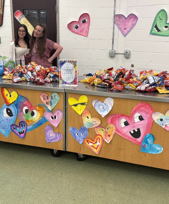 artwork display of student work and two teachers serving snacks