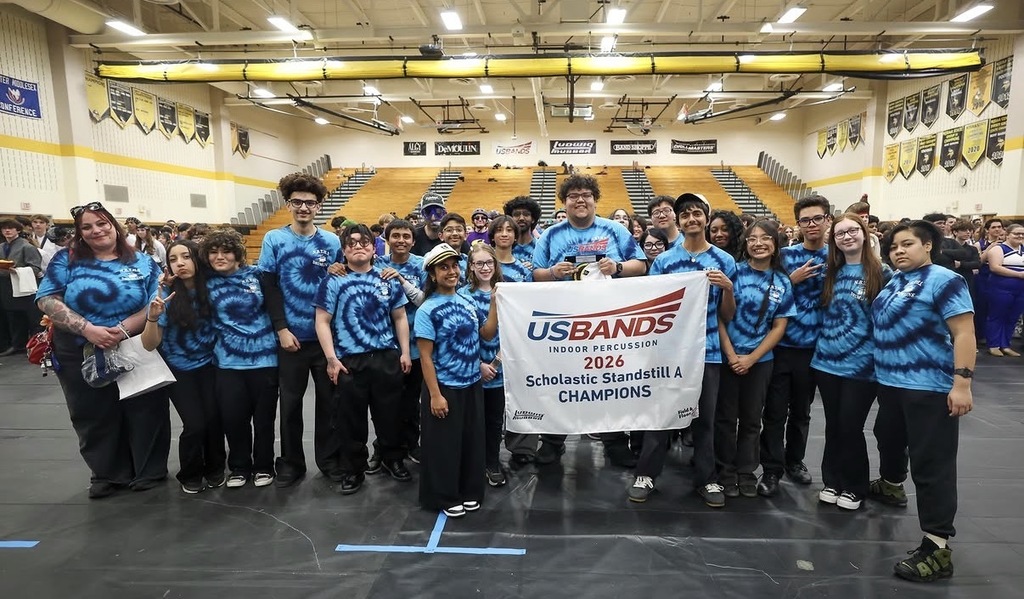 Members of the NBTHS Winter Percussion Ensemble pose with their championship winning banner after winning first place at the USBands Indoor Percussion Championship Show.