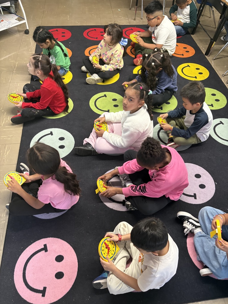 Students sitting on the carpet with pretend clocks