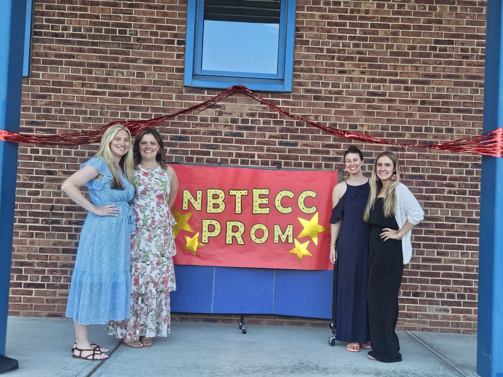 Teachers standing in front of an NBTECC PROM sign
