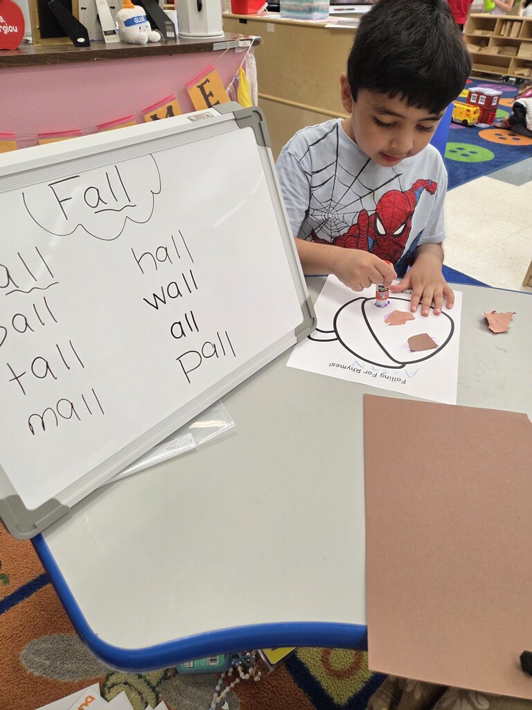 Fall words on a white board with a child gluing paper to an acorn paper